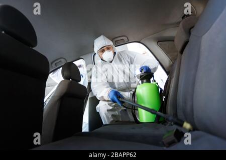 Uomo in tuta protettiva disinfettando con prodotti chimici la sua auto Foto Stock