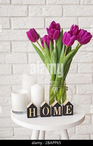 Tulipani viola in un vaso di vetro e lettere di legno disposte in una parola Home Foto Stock