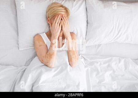 Donna che nasconde il suo viso con le mani e si posa a letto Foto Stock