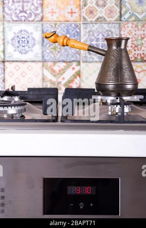 La cottura del caffè su un fornello a gas. Vecchio turco paiolo in rame per preparare il caffè sulla stufa in cucina. La colazione anticipata. Bagno turco metodo di preparazione del caffè. Foto Stock