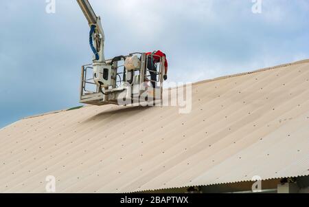 I lavoratori nella rampa di sollevamento idraulica riparano il gocciolatoio del tetto. Costruttori su piattaforma di sollevamento del braccio in piedi vicino alla parete dell'edificio, costruzione e riparazione w Foto Stock