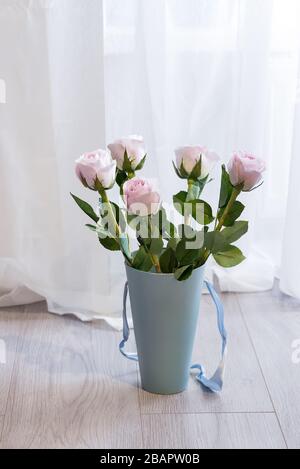 Bellissimo bouquet di rose rosa in una scatola blu regalo sul pavimento vicino alla finestra e tende Foto Stock