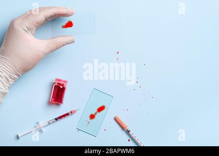 tecnico di laboratorio che gocciola sangue rosso umano sul vetrino per un test antivirus su sfondo blu Foto Stock