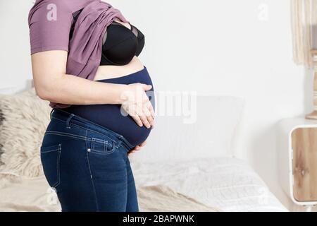 Pantaloni per donne in gravidanza. Fascia elastica speciale per il pancino, donna in camera da letto, vista laterale, copyspace Foto Stock