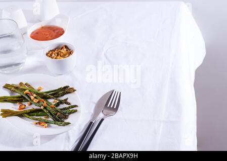 Asparagi arrostiti in olio d'oliva con noci tritate e salsa su un piatto bianco. Cibo vegetariano. Foto Stock