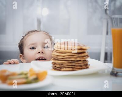 Messa a fuoco selezionata. Piccolo bambino che guarda frittelle fatte in casa con miele sul tavolo Foto Stock