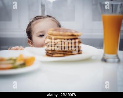 Messa a fuoco selezionata. Piccolo bambino che guarda frittelle fatte in casa con miele sul tavolo Foto Stock