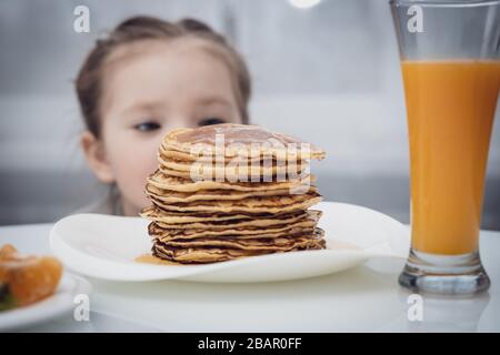 Messa a fuoco selezionata. Bambina che guarda frittelle fatte in casa con miele sul tavolo Foto Stock