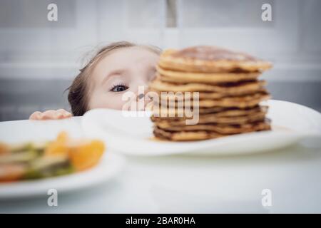 Messa a fuoco selezionata. Piccolo bambino che guarda frittelle fatte in casa con miele sul tavolo Foto Stock