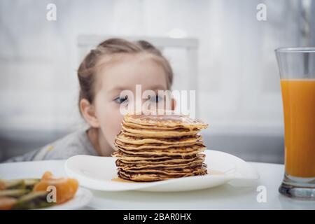 Messa a fuoco selezionata. Piccolo bambino che guarda frittelle fatte in casa con miele sul tavolo Foto Stock