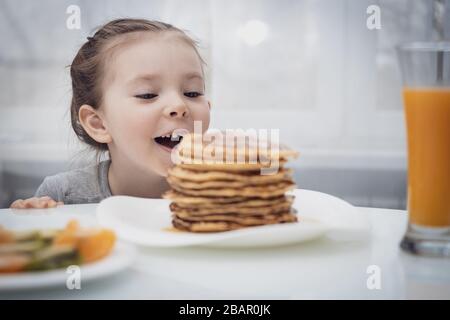 Messa a fuoco selezionata. Bambina che guarda frittelle fatte in casa con miele sul tavolo Foto Stock