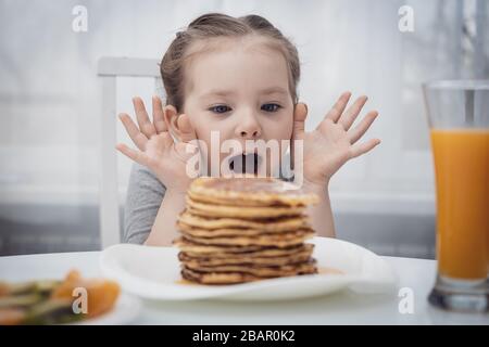 Messa a fuoco selezionata. Bambina che guarda frittelle fatte in casa con miele sul tavolo Foto Stock