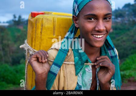 Una ragazza porta una lattina d'acqua attraverso un campo a Lalibela, regione di Amhara, Etiopia settentrionale Foto Stock