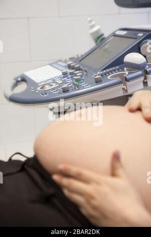 Vista su apparecchio ecografico, pancia di una donna incinta in primo piano non in primo piano, pancia femminile con le mani Foto Stock