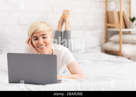 Donna di mezza età sorridente che usa un computer portatile mentre lavora a casa Foto Stock
