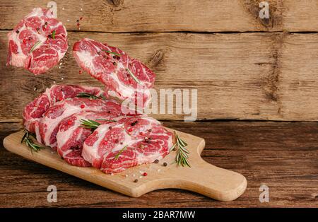 Bistecche di maiale al volo a bordo con carne e spezie su sfondo di legno. Spazio di copia Foto Stock