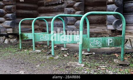 antico parcheggio arrugginito in bicicletta fatto di tubi piegati in metallo dipinto di verde, che si stacchino dal suolo senza una bicicletta in campagna vicino a una casa in legno. Foto Stock