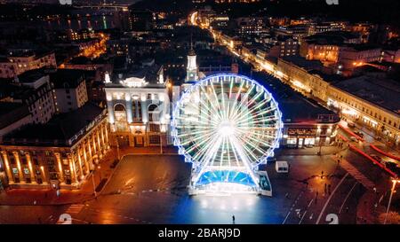 Splendida vista dal drone alla notte illuminata città di Kiev con ruota ferris in piazza. Foto Stock