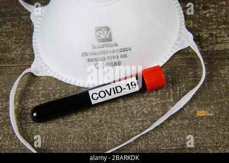 Viersen, Germania - 28.marzo 2020: Maschera ffp2 certificata CE isolata con fiala di campione di sangue covid-19 su tavola di legno Foto Stock