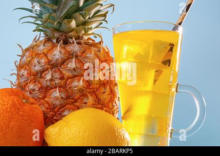 Succo di frutta multifrutta fresco con ghiaccio in un bicchiere. Ananas, arancia, limone, mela su sfondo blu Foto Stock