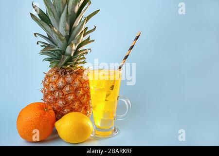 Succo di frutta multifrutta fresco con ghiaccio in un bicchiere. Ananas, arancia, limone, mela su sfondo blu Foto Stock