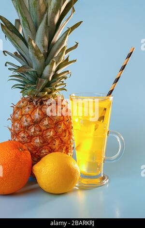 Succo di frutta multifrutta fresco con ghiaccio in un bicchiere. Ananas, arancia, limone, mela su sfondo blu Foto Stock