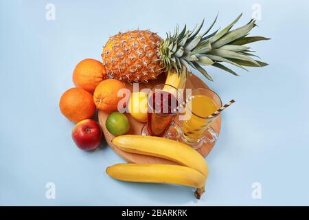 Succo di frutta multifrutta fresco con ghiaccio in un bicchiere. Ananas, arancia, banana, limone, mela su sfondo blu Foto Stock