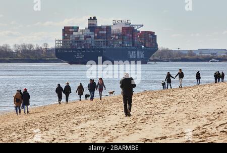 Amburgo, Germania. 29 marzo 2020. Gli escursionisti camminano lungo la spiaggia dell'Elba Övelgönne, mentre sullo sfondo la nave container YM wellhead sta navigando a valle. Credit: Georg Wendt/dpa/Alamy Live News Foto Stock