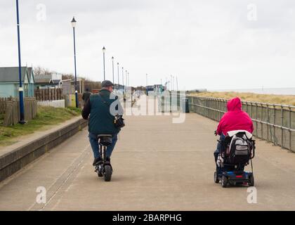 Coppia su scooter da mobilità lungo la passeggiata Sutton on Sea, Lincolnshire, Regno Unito Foto Stock