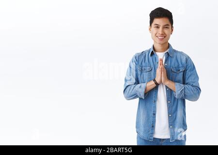 Ritratto di bel giovane studente maschio sorridente, ringraziando per l'aiuto, tenere le mani in preghiera, avere fede o speranza, stare in piedi sfondo bianco, apprezzare l'aiuto Foto Stock