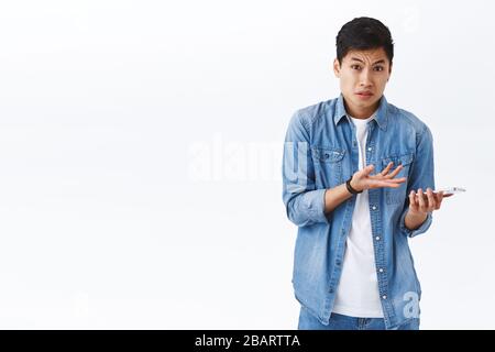 Tecnologia, concetto di stile di vita online. Ritratto di giovane frustrato e dispiaciuto lamentando l'uomo asiatico che punta al telefono cellulare con sgomento e Foto Stock