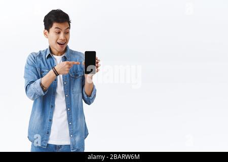 Tecnologia, concetto di stile di vita online. L'uomo felice sorpreso ed eccitato riceve l'invito via messaggio, puntando il dito verso il telefono mobile e sorridendo Foto Stock