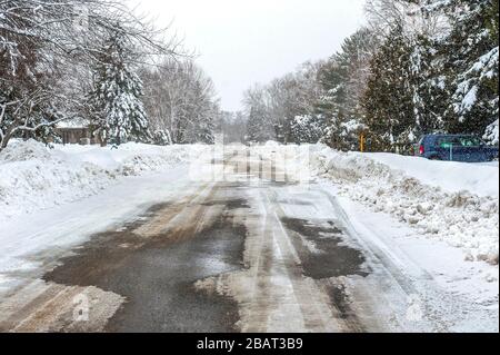 Strada suburbana parzialmente coperta di neve Foto Stock