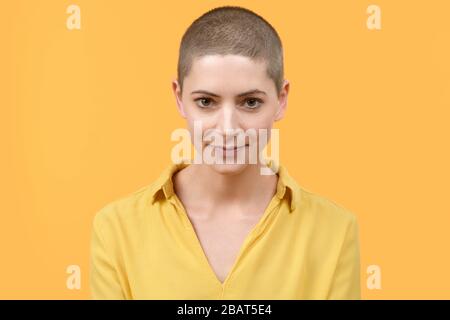 Studio ritratto di una bella giovane donna caucasica con testa rasata su sfondo giallo brillante. Cancro superstite ritratto. Foto Stock