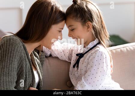 Giovane madre sorridente che tocca le fronte con figlia felice del bambino. Foto Stock