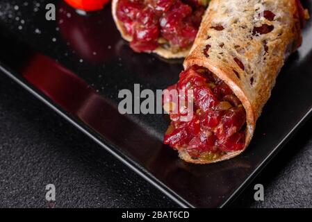 Delizioso tartaro di manzo fresco con toast su un piatto quadrato nero su sfondo scuro Foto Stock