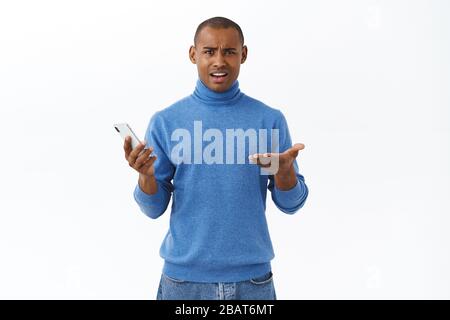 Tecnologia, concetto di stile di vita online. Ritratto del giovane afro-americano dispiaciuto che si è infradito in delusione, mantenendo il telefono cellulare Foto Stock