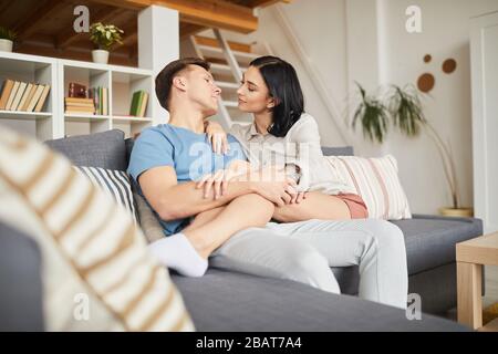 Ritratto di moderna giovane coppia coccolando mentre seduto sul divano in casa accogliente interno, copia spazio Foto Stock