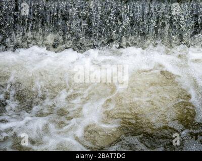 Acqua che scorre in una piccola cascata schiumosa e schiumosa Foto Stock