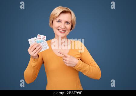 Donna di media età sorridente, indicando le pillole in blister confezione Foto Stock