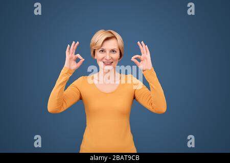 Stile libero. Donna matura in piedi isolata in blu mostrando zen gesto felice Foto Stock