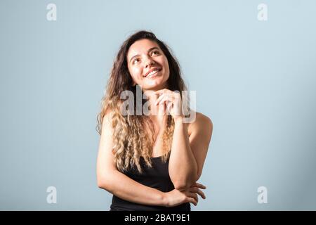 ritratto di tenera giovane donna con capelli ricci sorridenti e toccante il viso su sfondo blu Foto Stock