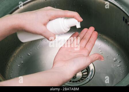 Protezione delle mani da virus, influenza e batteri. Donna mette schiuma da uno spray bianco può sulle sue mani. Lavare a mano nel lavandino Foto Stock