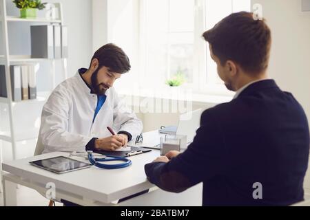 Il paziente visita il medico presso l'ufficio della clinica. Il lavoro medico scrive una prescrizione su un tavolo in un ospedale. Foto Stock