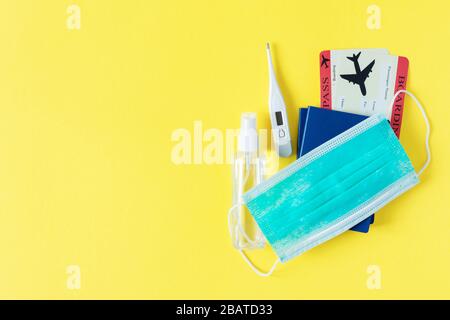 Virus e concetto di viaggio. Passaporto e carta d'imbarco con maschera chirurgica, gel igienizzante con alcol e termometro su sfondo giallo vista dall'alto. Protezione Foto Stock