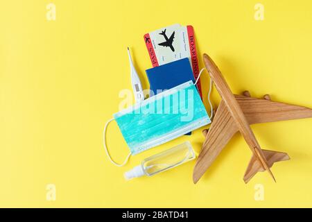 Virus e concetto di viaggio. Passaporto e carta d'imbarco con maschera chirurgica, gel igienizzante con alcol e termometro su sfondo giallo vista dall'alto. Protezione Foto Stock