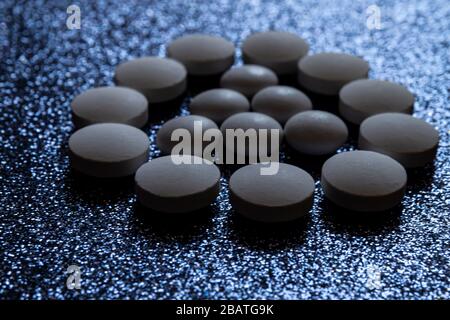 Pillole bianche, compresse capsule formano un triangolo in un cerchio su uno sfondo scuro lucido. Foto Stock