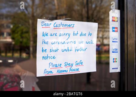 Avviso scritto a mano del cliente nella finestra del negozio di beneficenza Naomi House che consiglia la chiusura a causa di emergenza Coronavirus Foto Stock