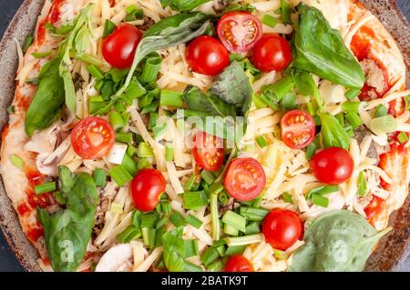 Pizza fresca cruda con funghi, pomodori ciliegini, basilico e parmigiano. Pizza fatta in casa prima della cottura Foto Stock