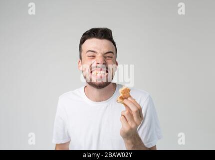 Giovane uomo isolato sullo sfondo. Allegro felice ma strano ragazzo sorridente largo e mostrando denti con hamburger tra di loro. Gustoso delizioso e. Foto Stock